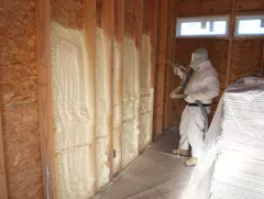 Technicians installing spray foam insulation in a wall.