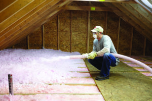 Pink fiberglass loose-fill insulation being installed in attic