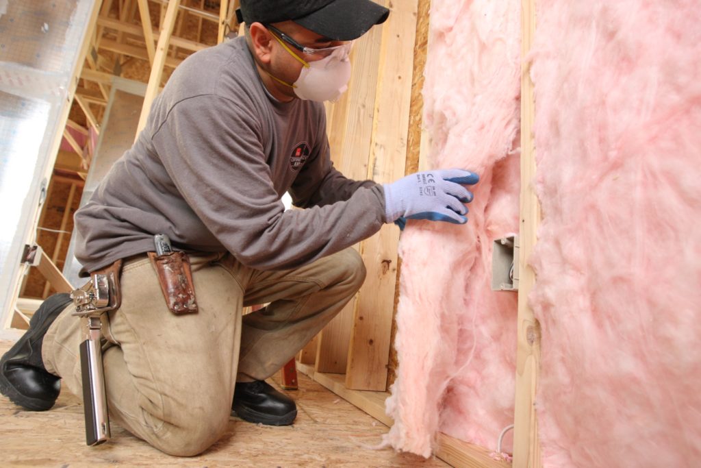 Technician installing pink fiberglass batt rolls into wall.