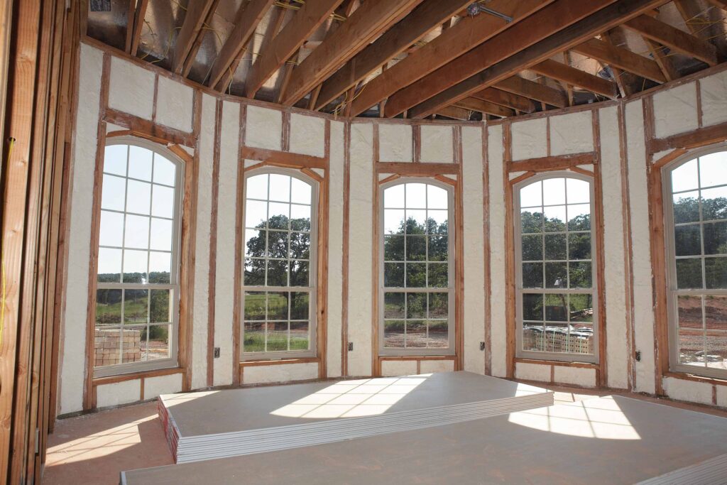 Spray foam insulation inside a new home, around a curved wall of tall windows.